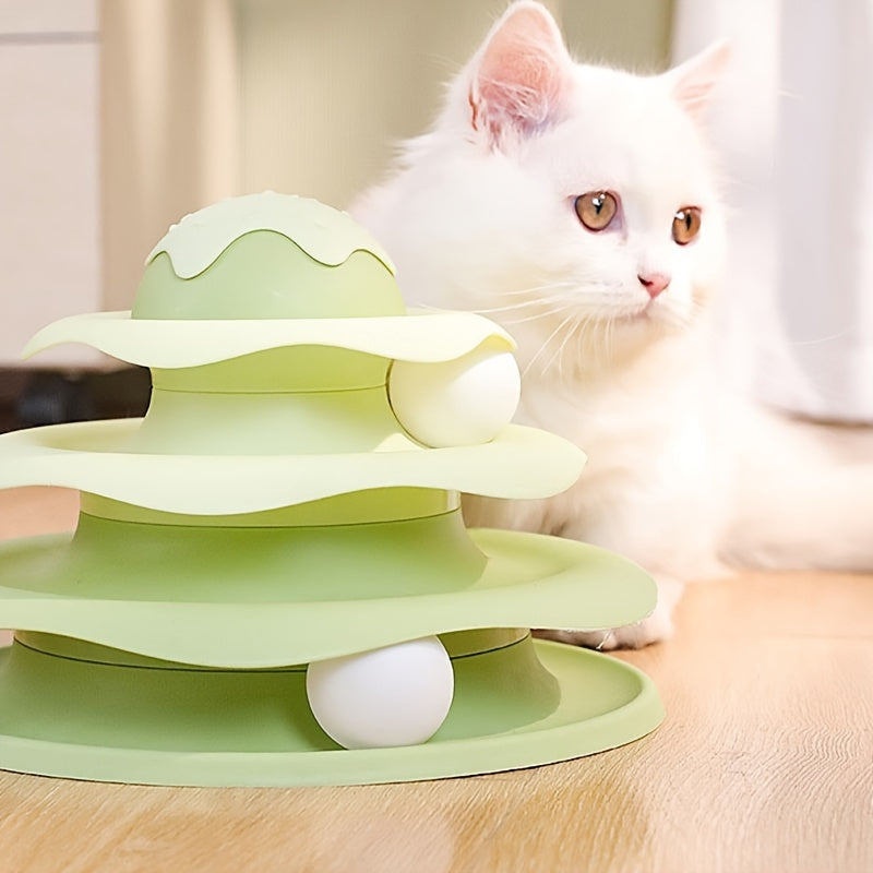 Green three-tiered cat toy with a white cat sitting next to it on a wooden surface.