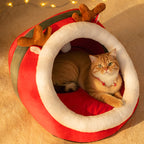 Cat lying in a red and white pet bed with reindeer antlers on a beige background.