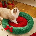 Cat on a green and red wreath-shaped pet bed with Christmas decorations in the background.