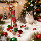 Cat sitting on a blanket with Christmas decorations and a toy in front of a decorated tree.