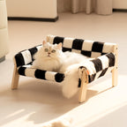 Cat lounging on a black and white checkered pet bed with wooden frame.