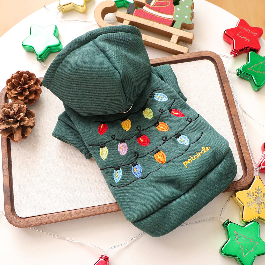 Green hoodie with Christmas lights design on a wooden tray with decorative items.