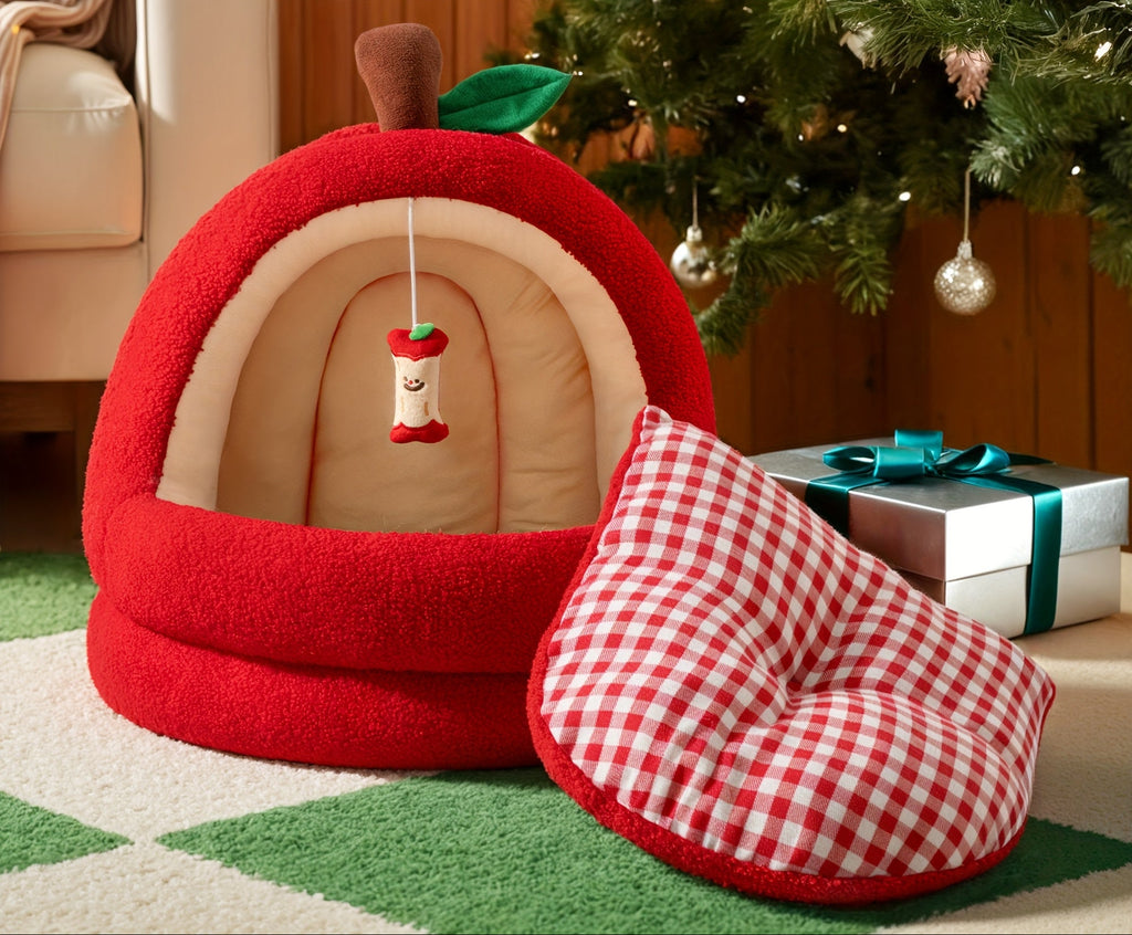 Red and beige pet bed with checkered pillow on a green carpet, Christmas tree, and presents in the background.