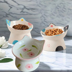 Three cat-shaped ceramic bowls with pet food on a marble surface.