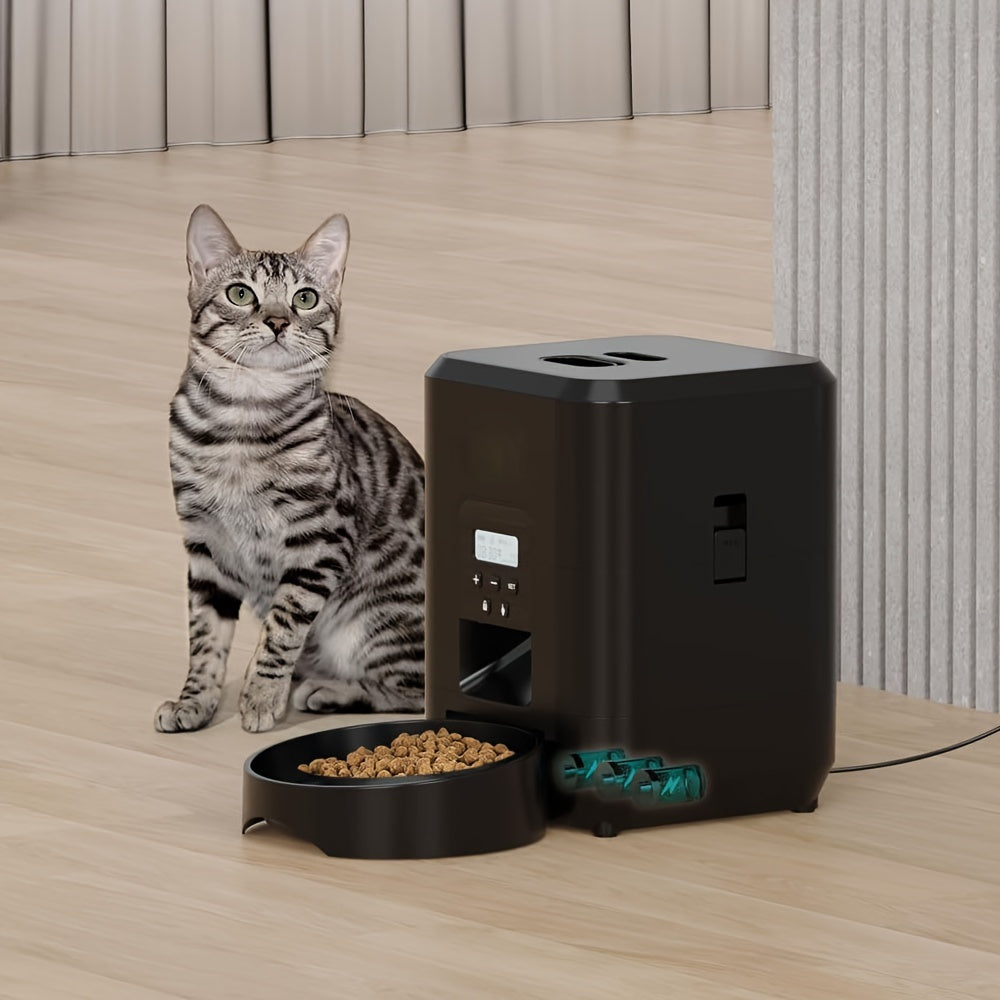 Cat sitting next to a black pet feeder on a wooden floor.