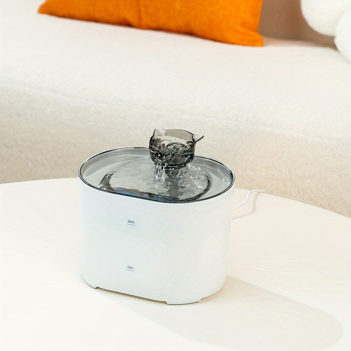 Pet water fountain on a white surface with an orange pillow in the background