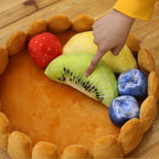 Toy fruit set with a hand pointing to a kiwi slice on a wooden surface