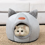 Cat peeking out from a gray pet house with cat ears on a beige carpet.