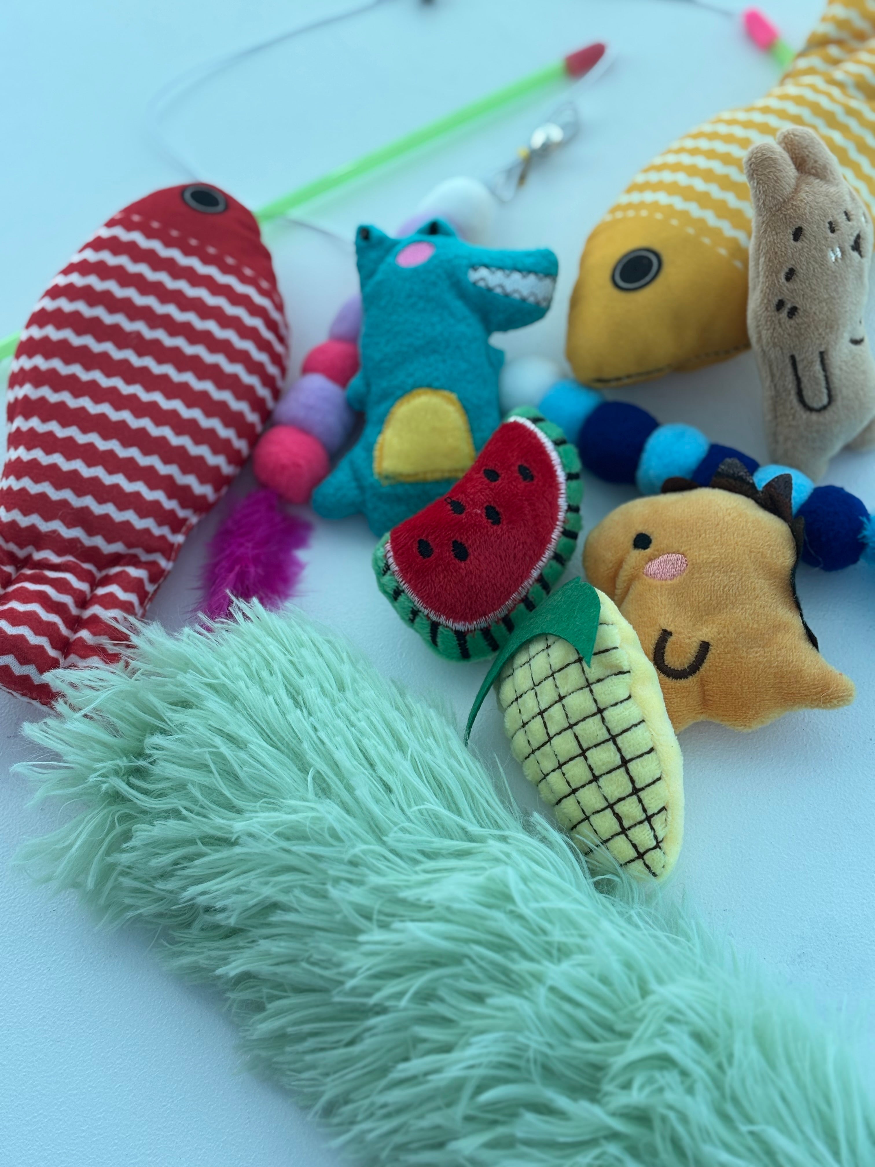 Assorted cat toys including fish, watermelon, corn, and mouse shapes on a white background.
