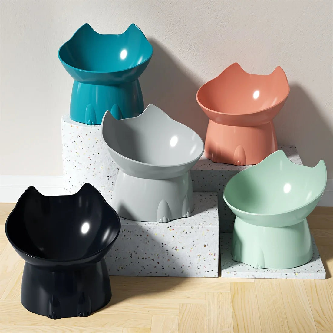 Five colorful cat-shaped bowls on a wooden surface with a light gray background