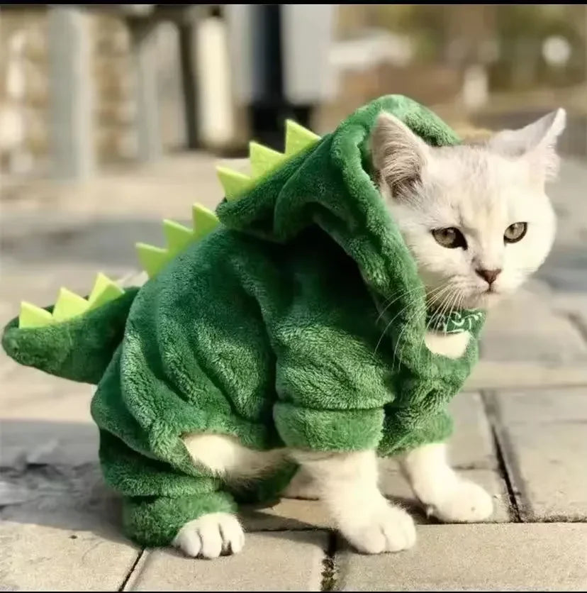 Cat wearing a green dinosaur costume on a wooden floor.