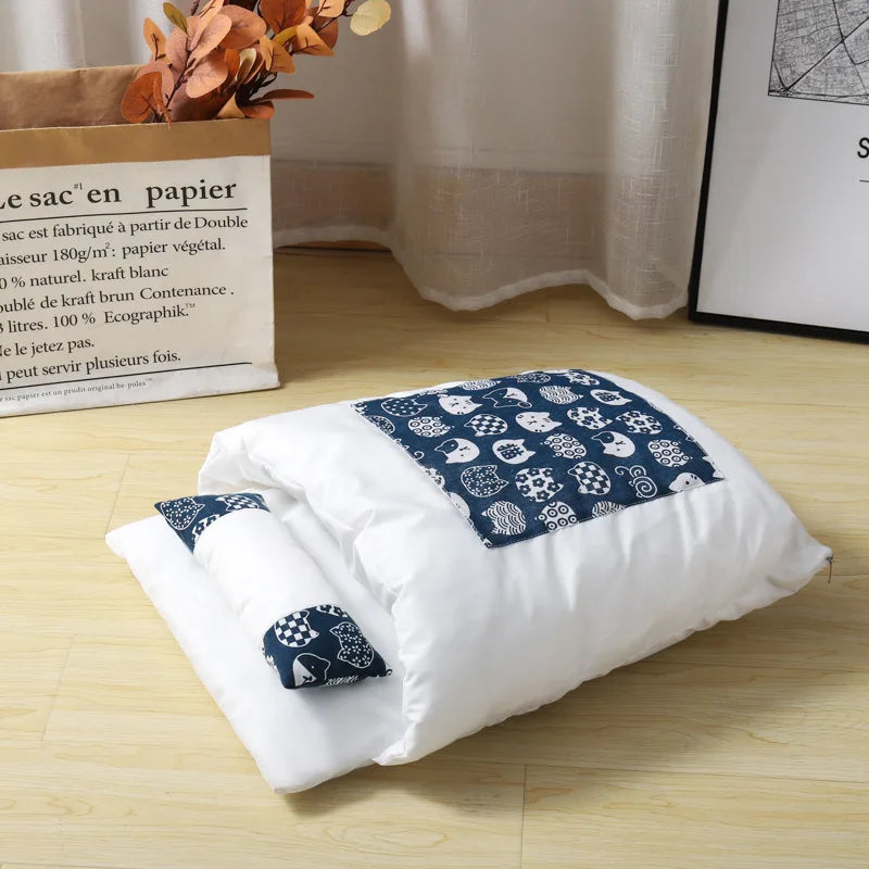 White quilt with blue patterned ends on a wooden floor, with a box and plant in the background.