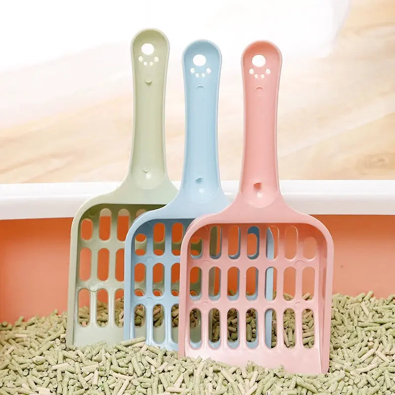Three colorful cat litter scoops on a bed of cat litter with a neutral background.