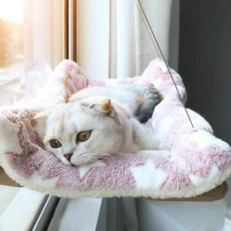 Cat lounging on a pink plush cat hammock with a blurred background