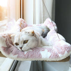 Cat lounging on a pink plush cat hammock with a blurred background