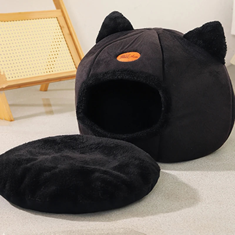 Black cat-shaped pet bed on a light gray floor with a wooden chair in the background.