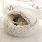 Two cats snuggled inside a plush, round pet bed on a soft white surface.
