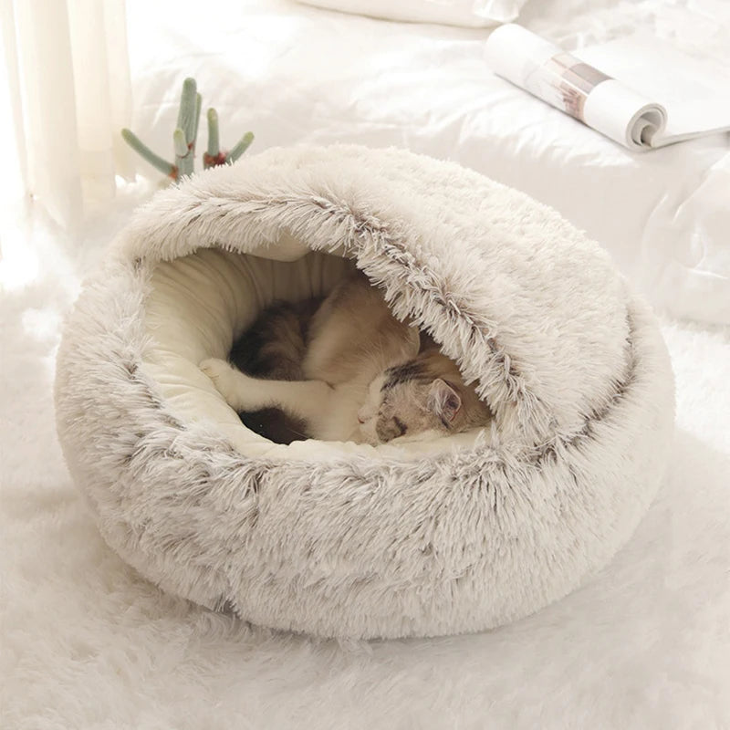 Two cats snuggled inside a plush, round pet bed on a soft white surface.
