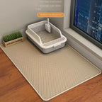 Cat litter box on a large beige mat in a room with a window and plant.