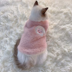 Cat wearing a pink fleece sweater with a heart design on a fluffy white surface