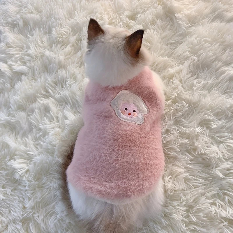 Small dog wearing a pink fleece sweater with a cartoon face on a fluffy white surface