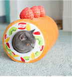 Gray cat interacting with a fruit-themed pet bed on a light blue carpet.