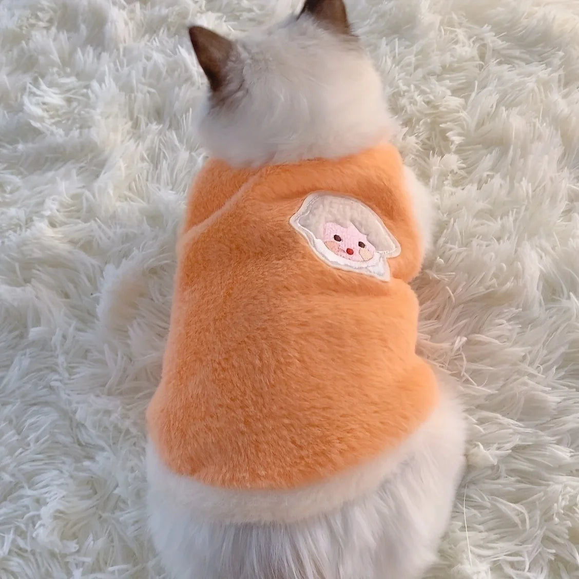 Cat wearing an orange fleece sweater with a paw print on a white fluffy surface
