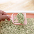 Pink cat litter scoop with green cat litter on a beige background