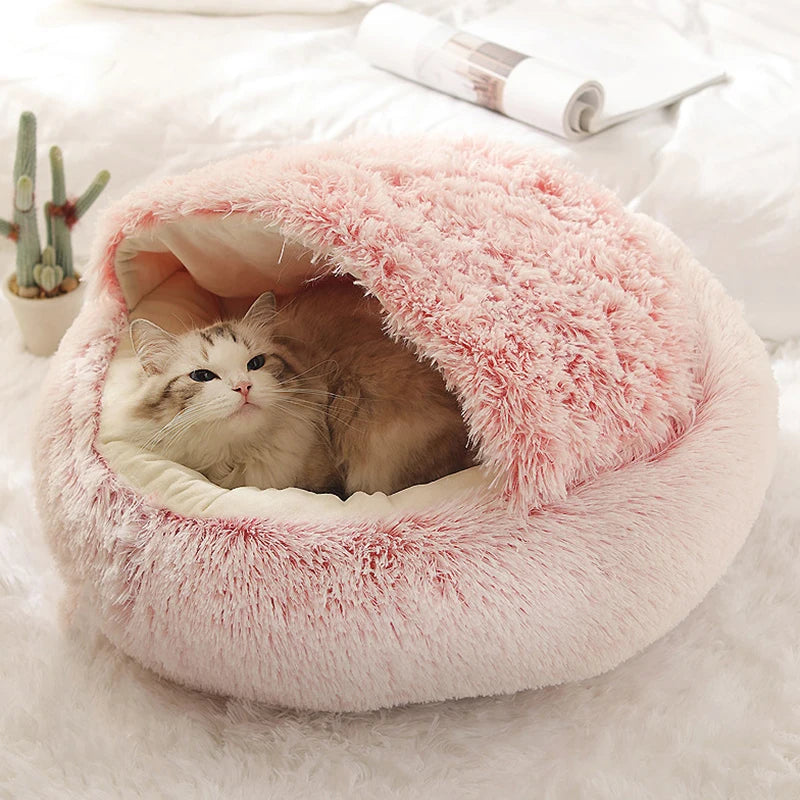 Cat lying in a fluffy pink pet bed on a white surface with a cactus plant in the background.