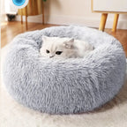 Fluffy gray pet bed with a white cat inside, on a light wooden floor.