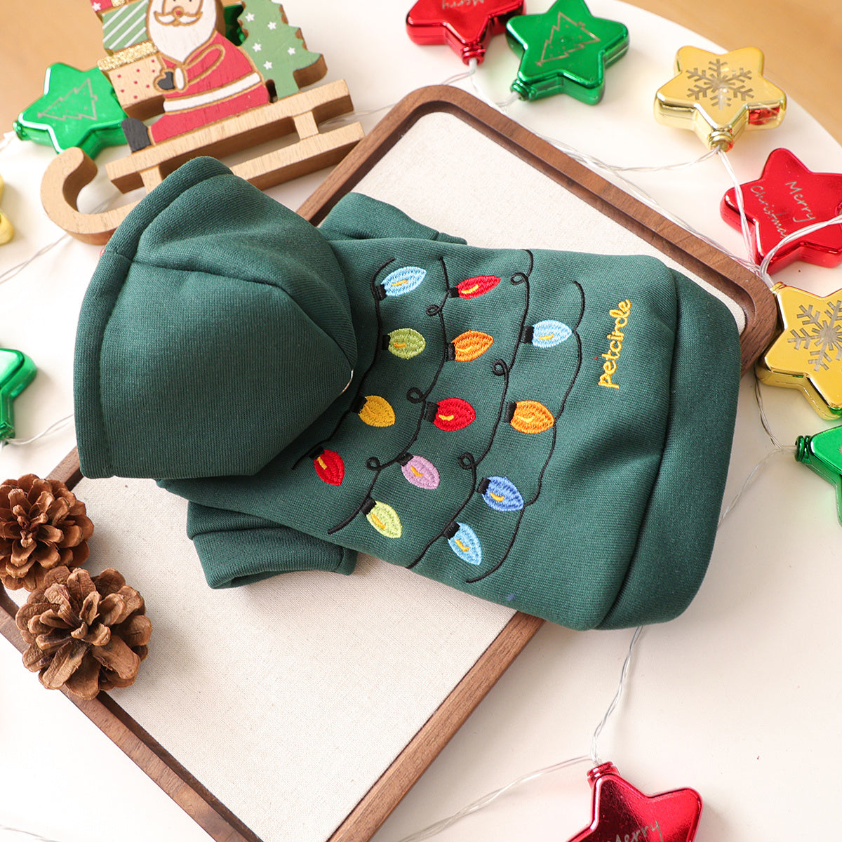 Green dog sweater with colorful lights design on a white surface with Christmas decorations.
