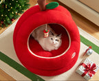 Red apple-shaped pet bed with a cat inside, Christmas tree and decorations in the background