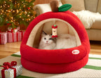 Red pet bed shaped like an apple with a cat inside, Christmas tree and presents in the background.