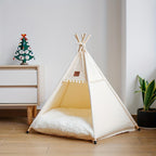 White pet teepee with a cushion on a wooden floor, next to a dresser and plant.