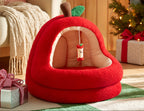 Red apple-shaped pet bed in a cozy living room with Christmas decorations.