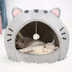 Cat lying inside a gray cat-shaped pet bed with a white paw toy hanging inside.
