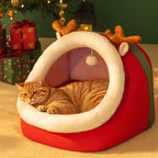 Cat lying in a red pet bed with reindeer antlers near Christmas presents.