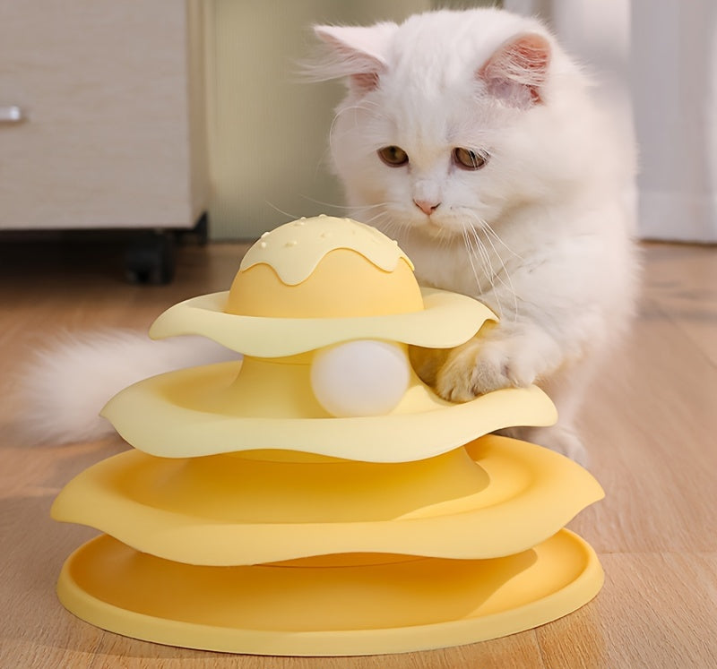 White cat playing with a yellow three-tiered pet toy on a wooden floor.